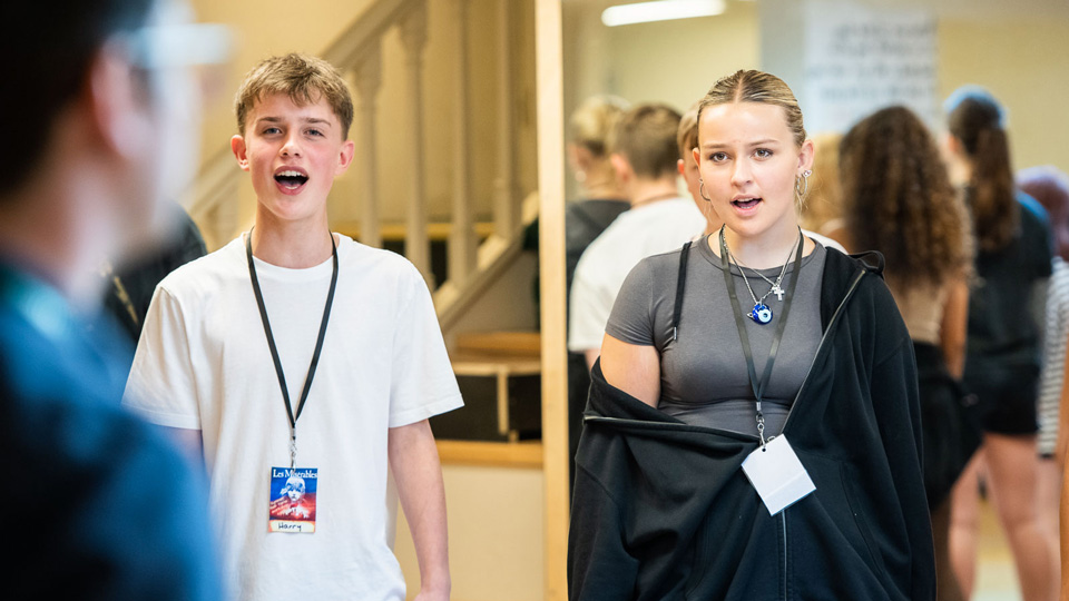 A boy and a girl aged about fourteen are singing, with a male workshop leader in the foreground.