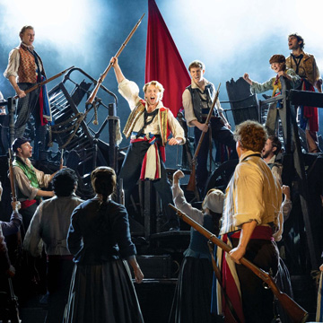 A photograph of the barricade scene from Les Miserables, including the character of Enjolrus surrounded by students.